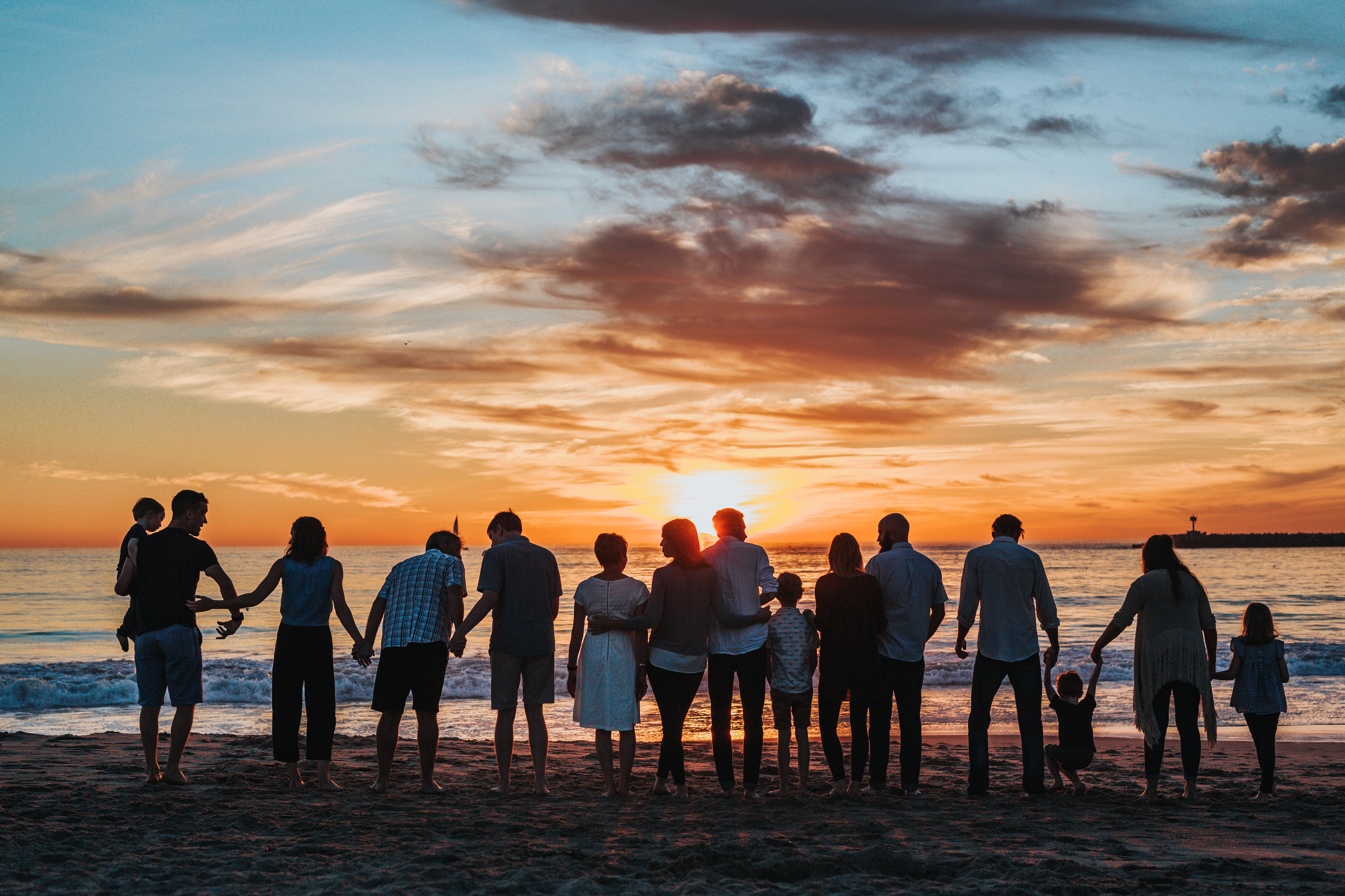 A group of people holding hands staring at a sunset in the sea