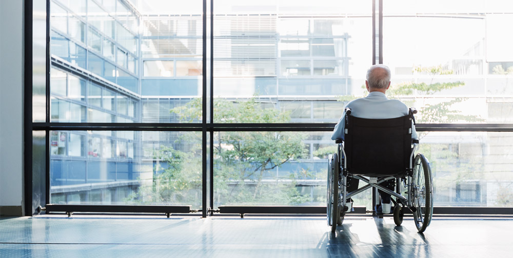 Man in wheelchair looking out of the window of a nursing home