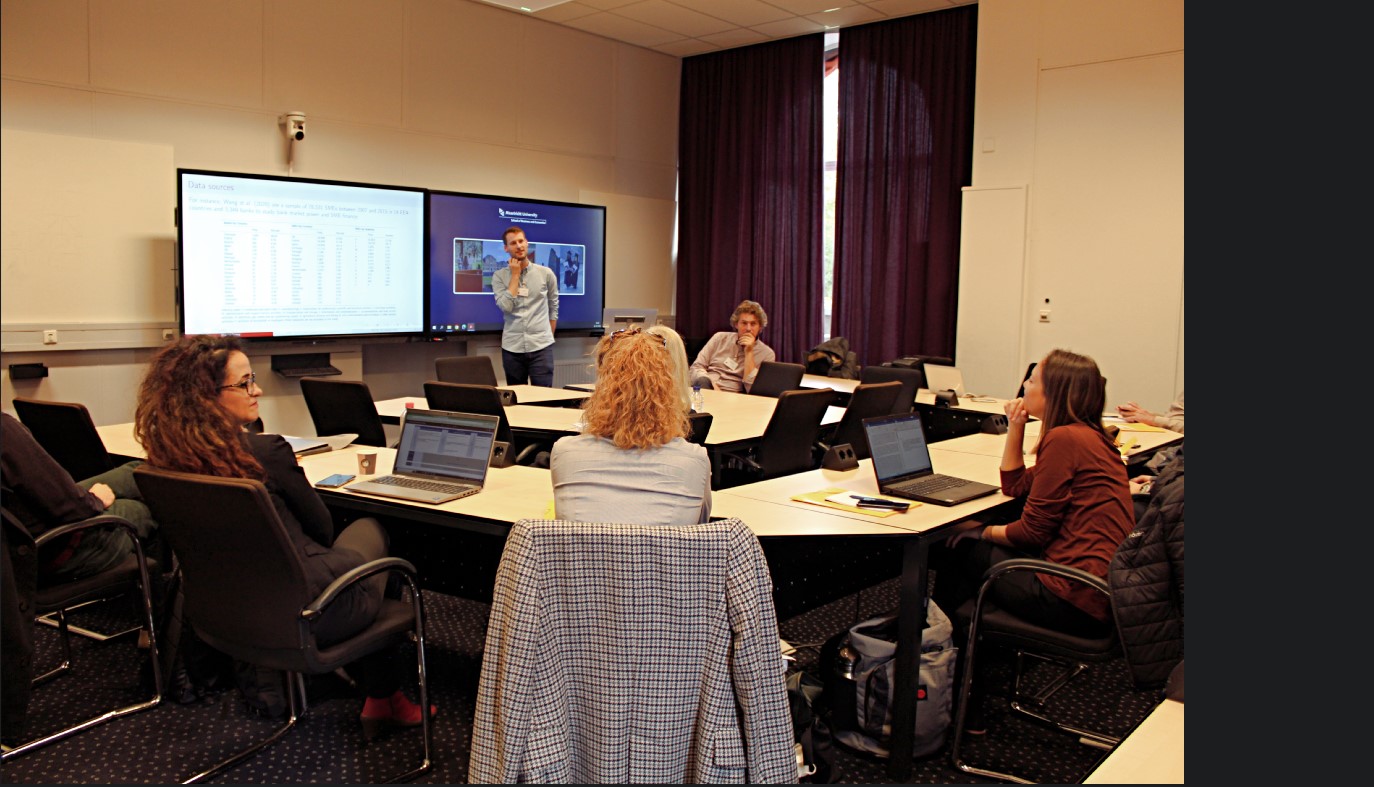 One person giving a presentation and people sitting around the room in a circle