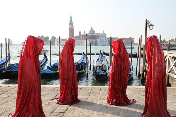 People with red cloaks on a quay in Venice