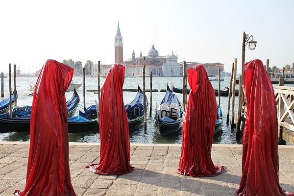 People with red cloaks on a quay in Venice