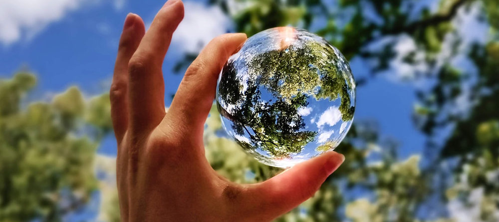 hand holding glass sphere towards sky