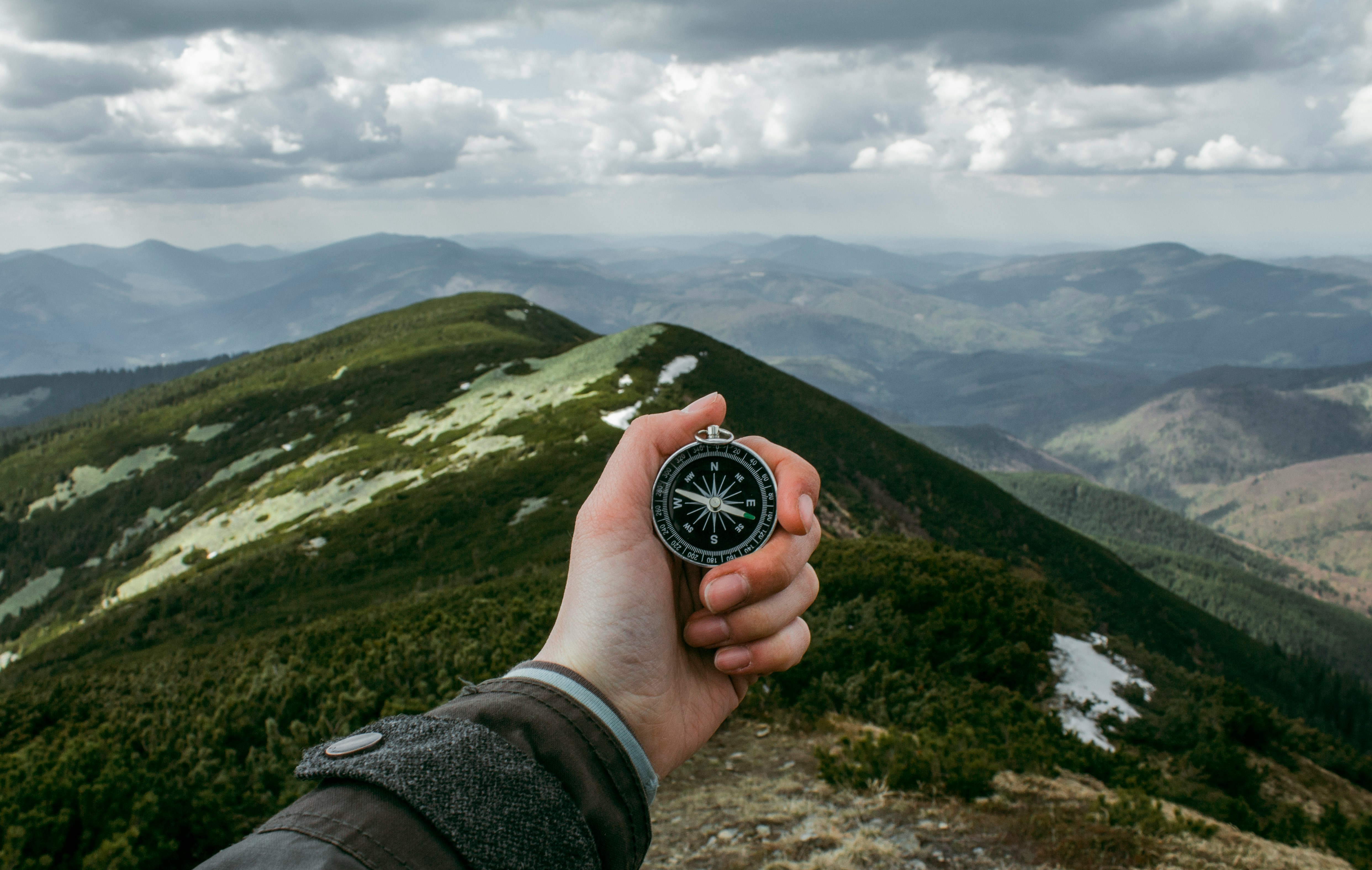 A hand holding a compass in the mountains