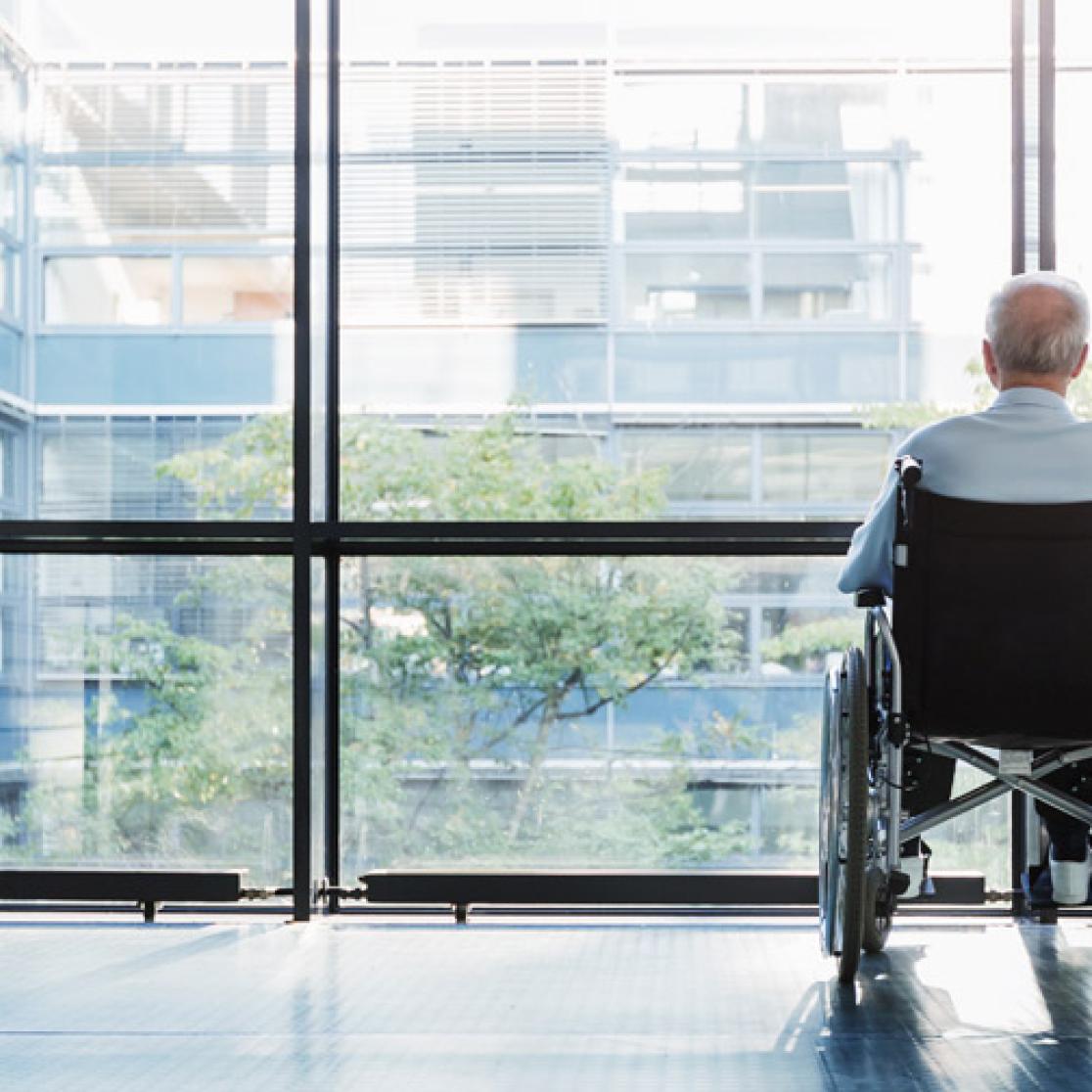 Man in wheelchair looking out of the window of a nursing home