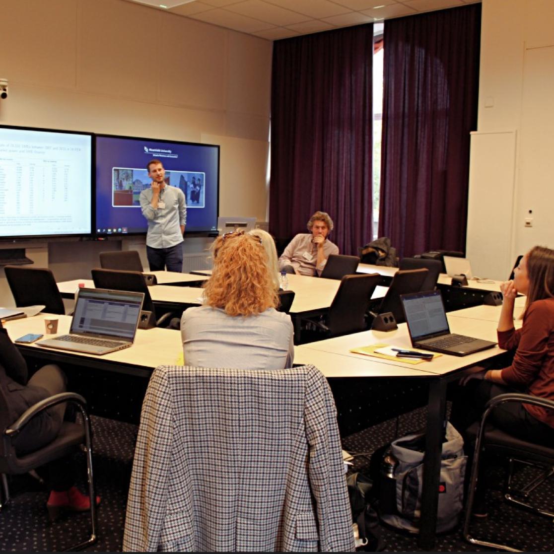 One person giving a presentation and people sitting around the room in a circle