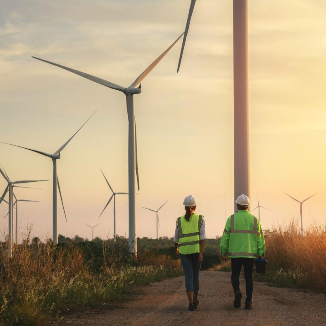 two people walking towards wind turbines