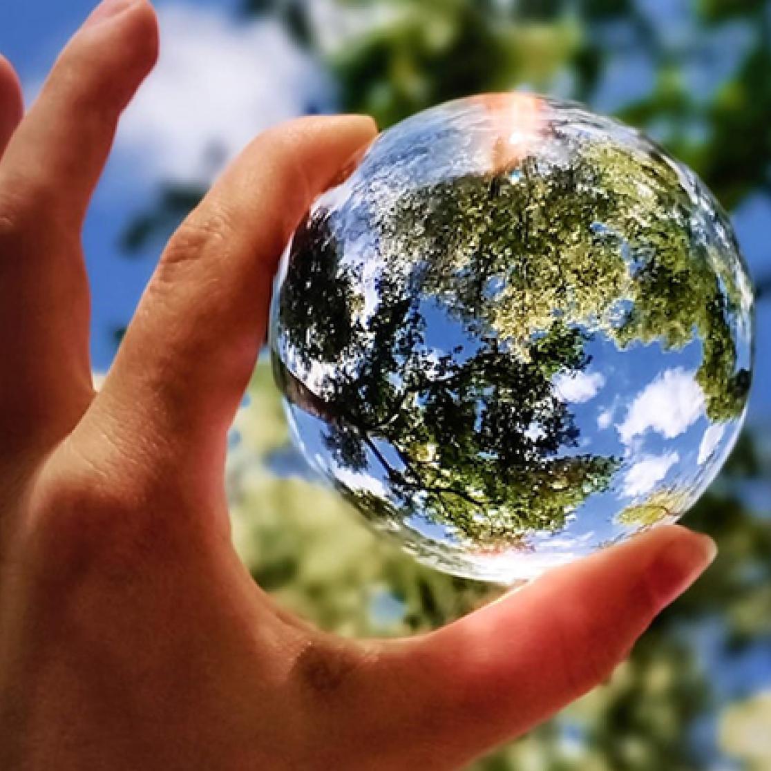 hand holding glass sphere towards sky