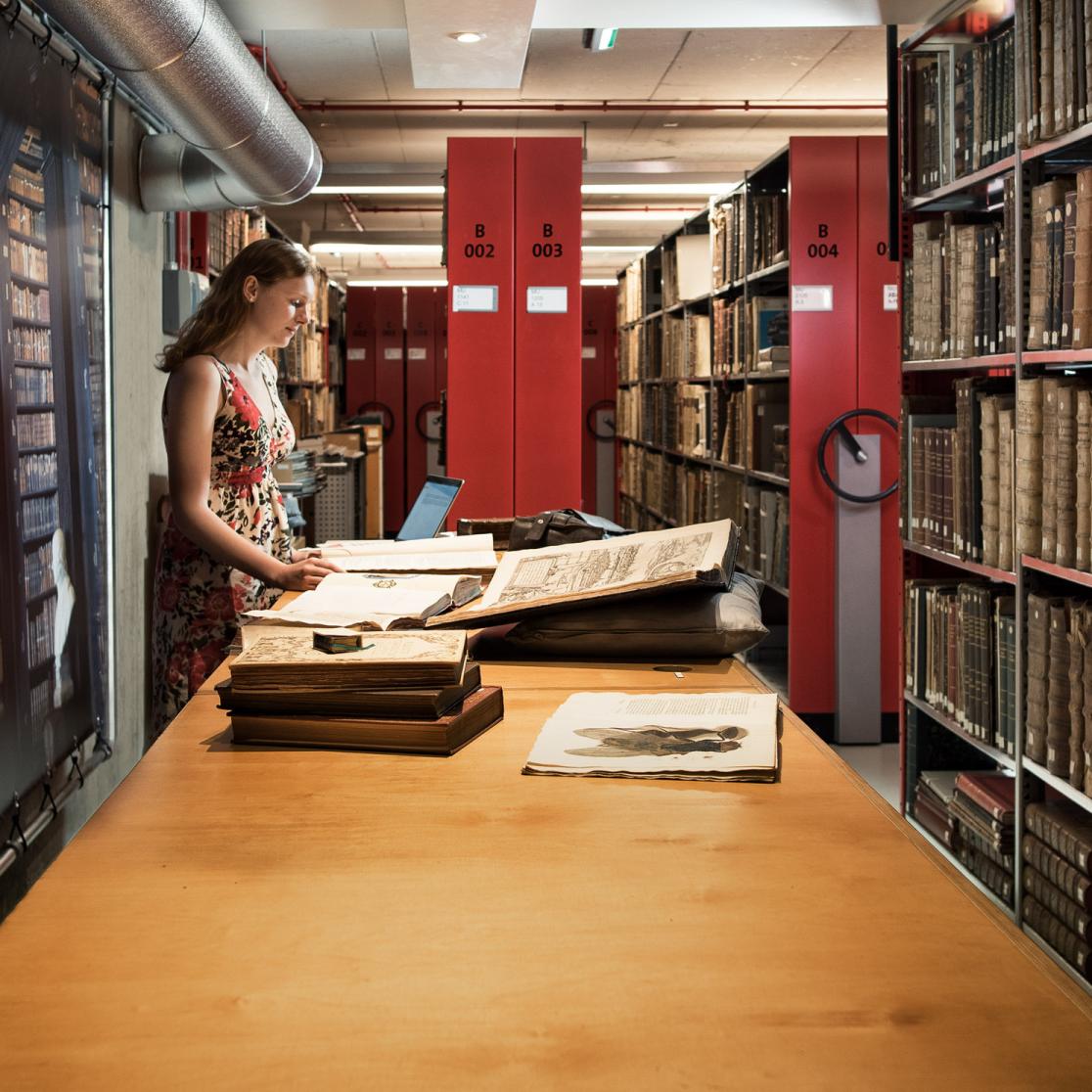 Person standing in the library looking into big books on a table