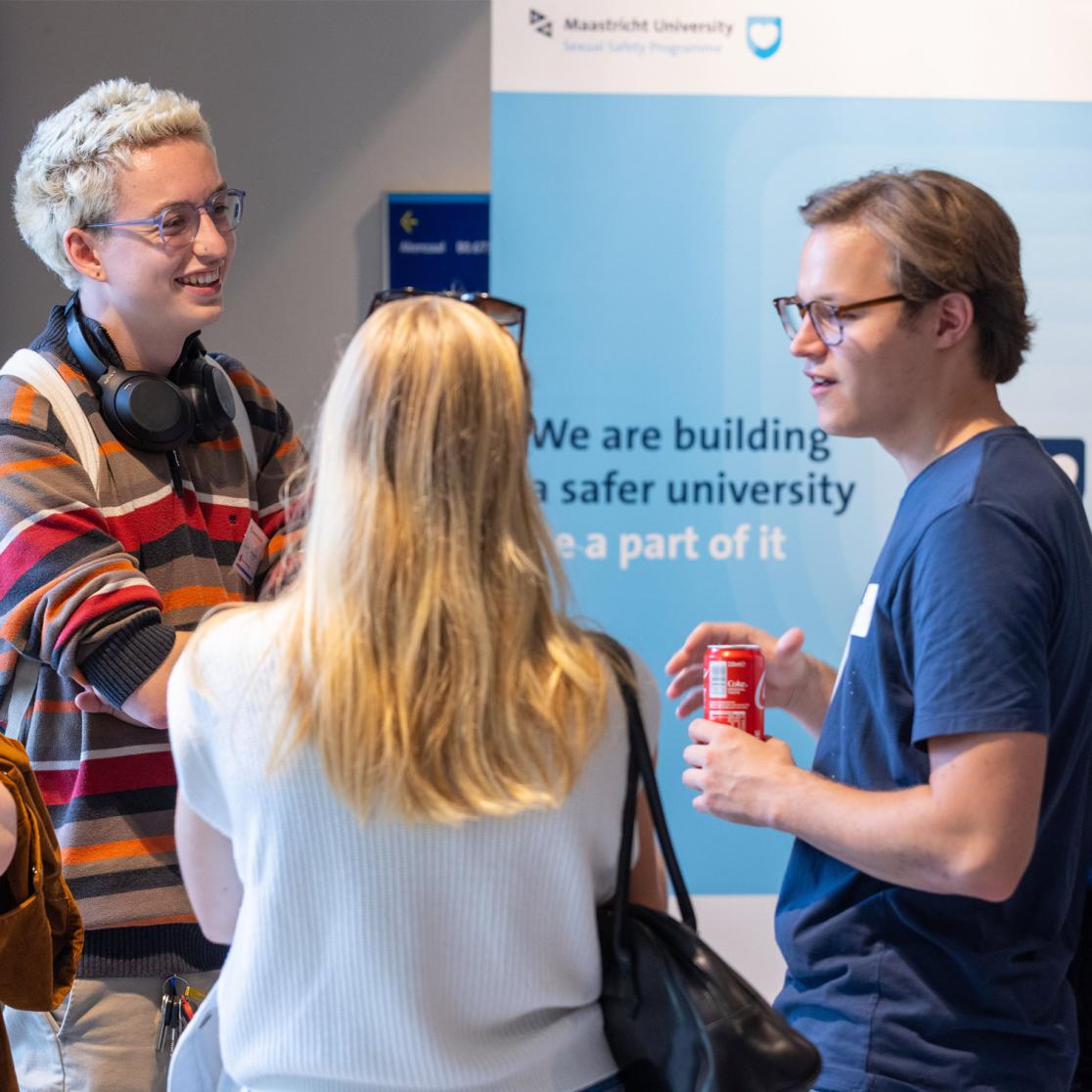 3 people having a conversation in front of a Universitiy banner