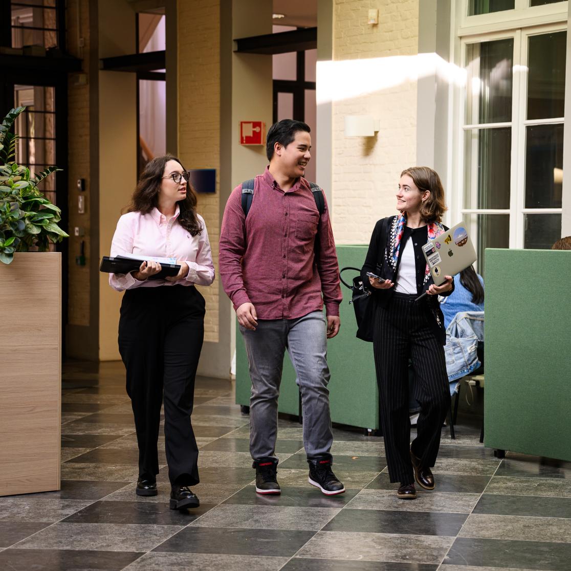 Three students smiling and walking through the Kapoenstraat campus building of the Faculty of Law.
