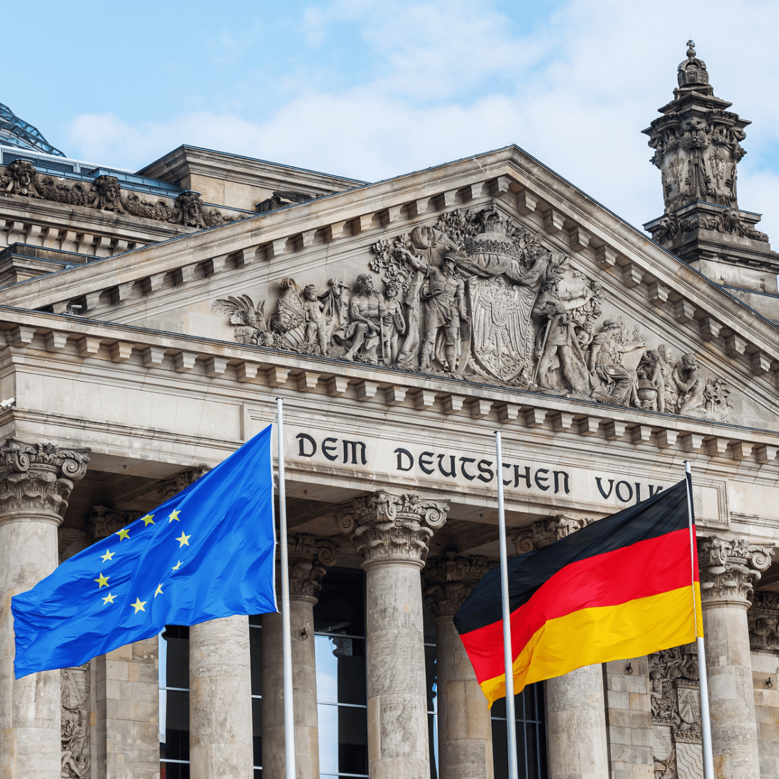 "The Reichstag building in Berlin, Germany, with the European Union and German flags waving in front. The inscription 'Dem Deutschen Volke' is visible on the facade."