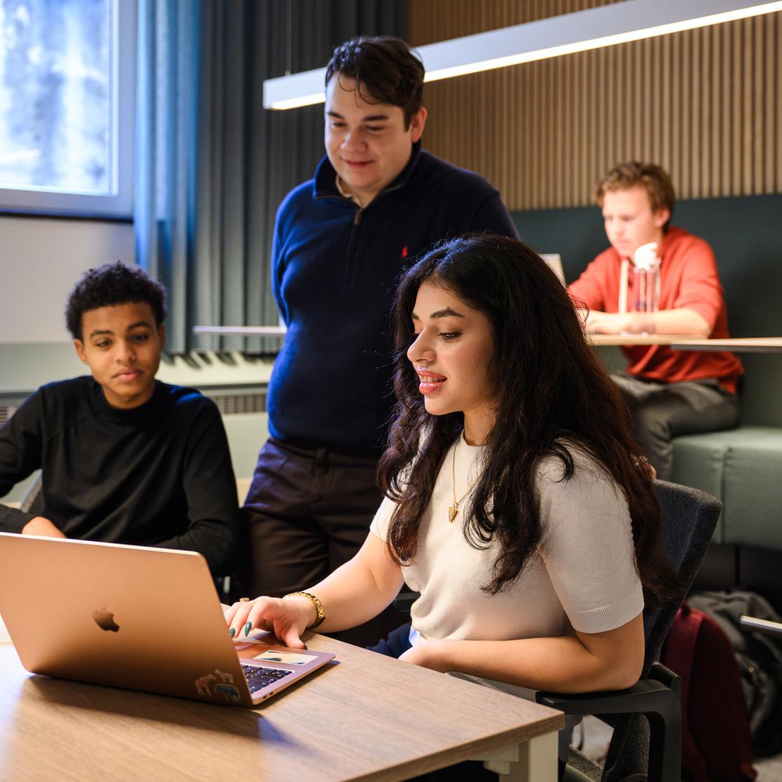 Three students are discussing something at a laptop in the faculty’s learning space, while others work independently in the background.