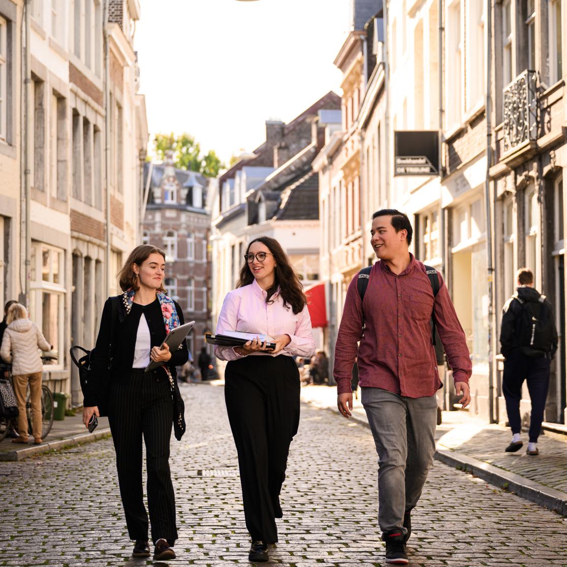 Drie studenten lopen door een zonovergoten straat in het centrum van Maastricht.