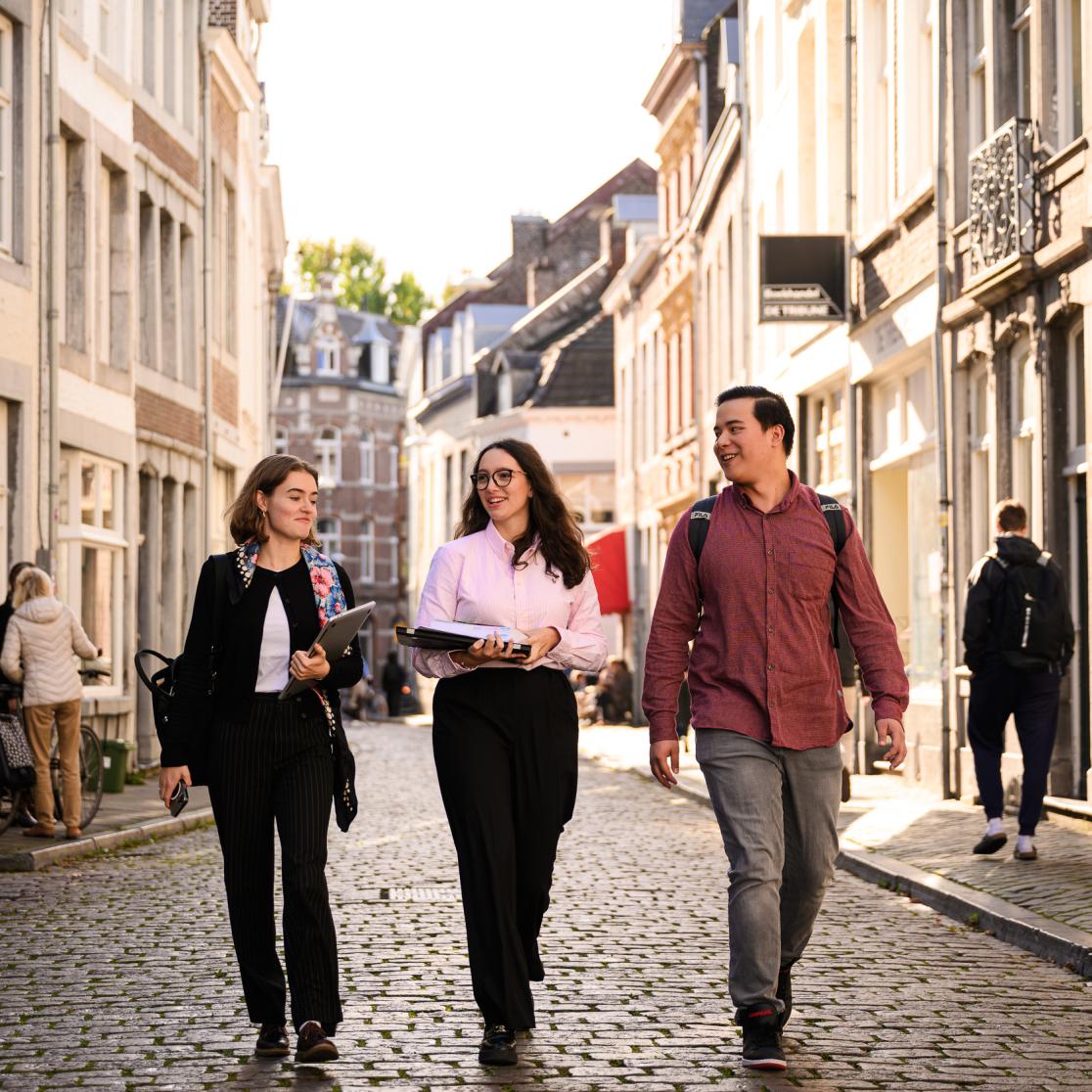 Drie studenten lopen door een zonovergoten straat in het centrum van Maastricht.