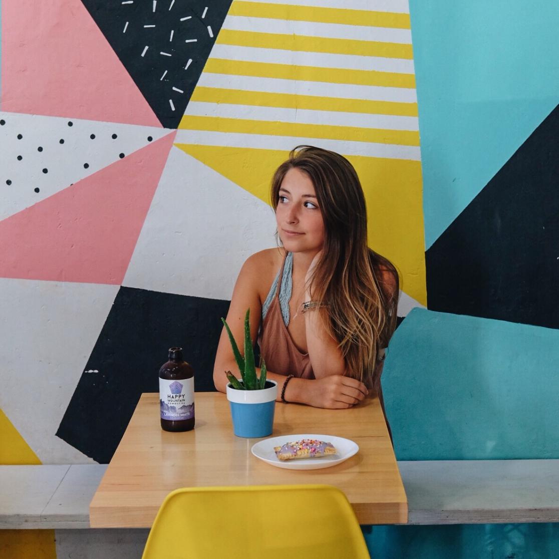 Becca sits in front of bright coloured wall