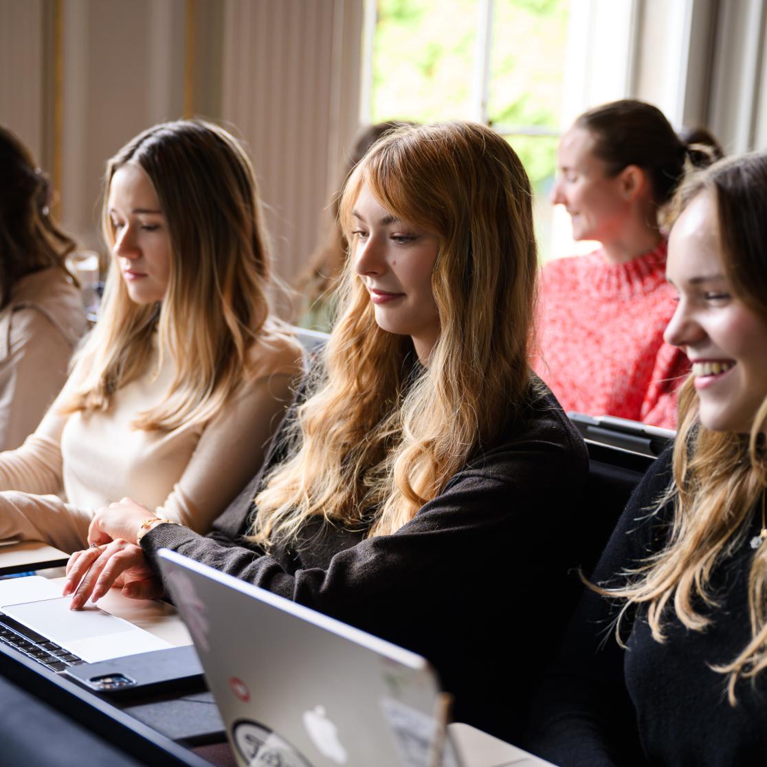 Studenten zitten zij aan zij in een collegezaal en werken op hun laptops tijdens het college.