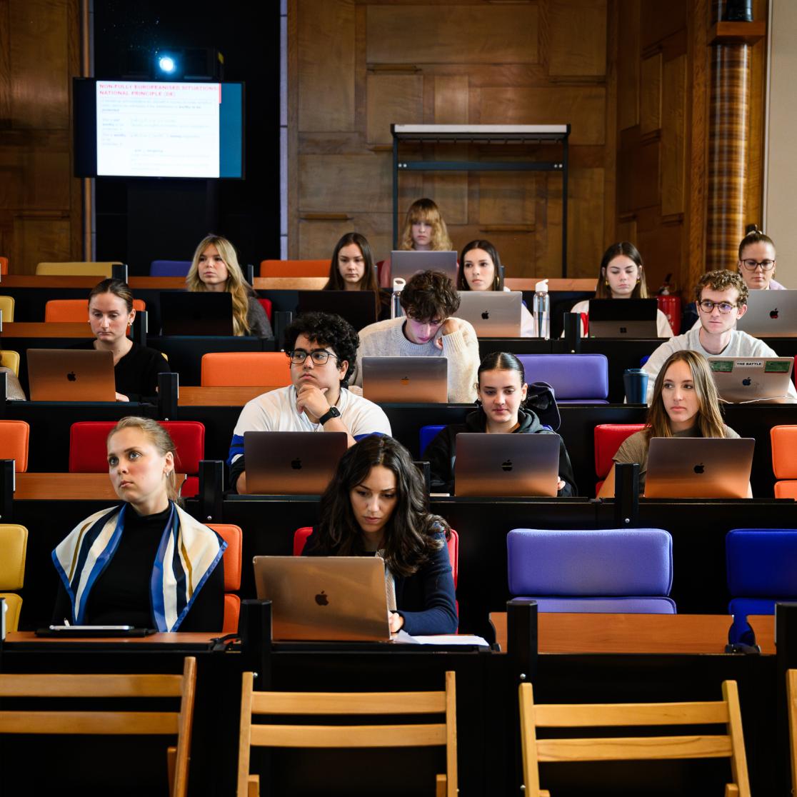 Students attend a lecture in a large faculty auditorium called the Statenzaal, taking notes on their laptops.