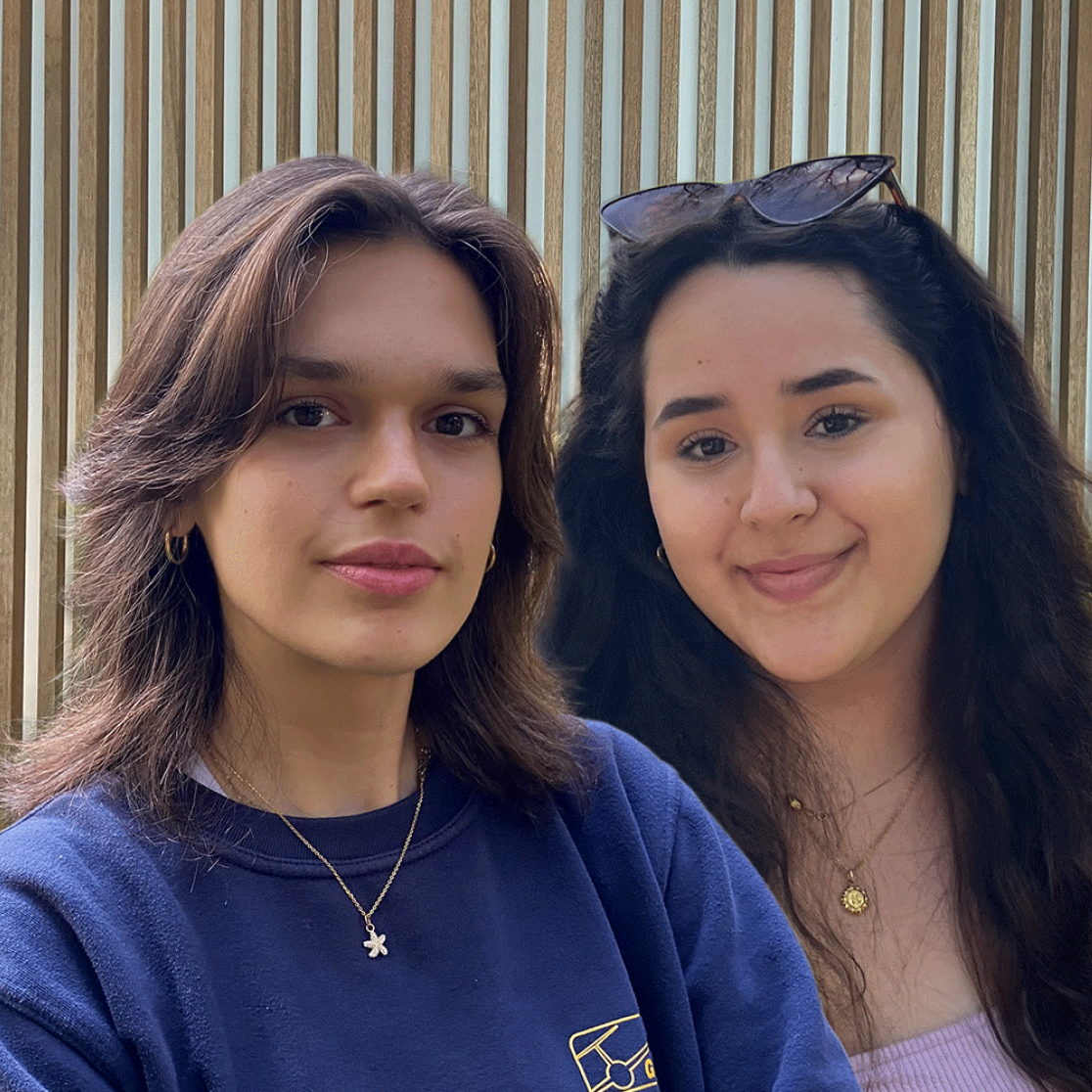 Two female students in front of wood panel wall