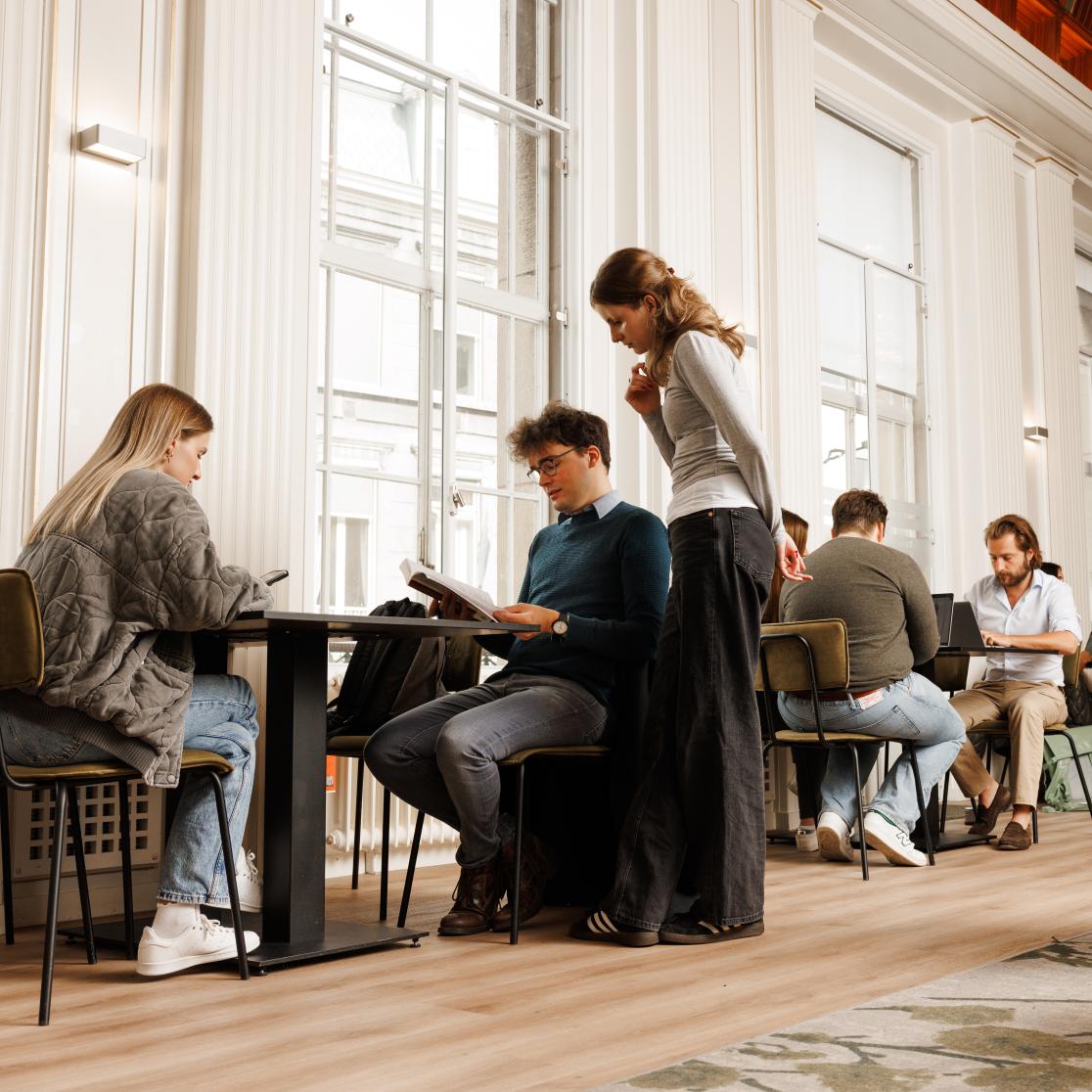 Studenten werken samen en studeren in een stijlvolle common room met hoge plafonds en veel daglicht.