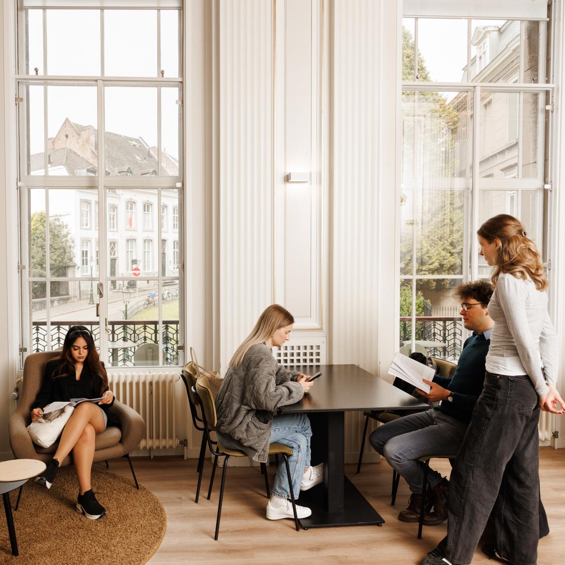 Studenten ontspannen en studeren in een lichte en elegante common room met uitzicht op de binnenstad van Maastricht.