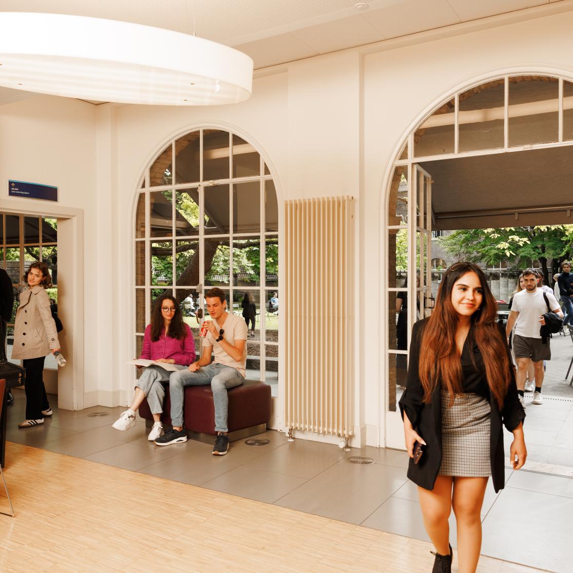 Students at the Faculty of Law’s Law Café: one student walks in while others are seated inside and outside, studying and relaxing.