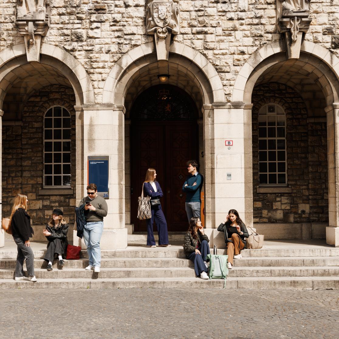 Students sitting and chatting on the steps of the historic entrance of the Faculty of Law on Lenculenstraat in Maastricht.
