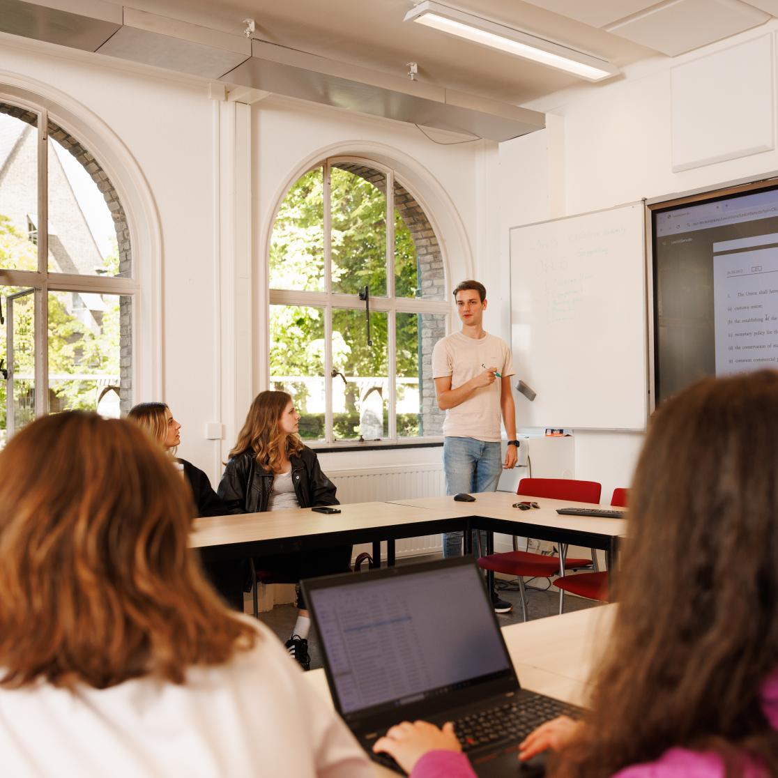 Student geeft een presentatie voor een groep medestudenten tijdens een PBL-sessie, met aantekeningen op het whiteboard en juridische tekst geprojecteerd op het scherm.