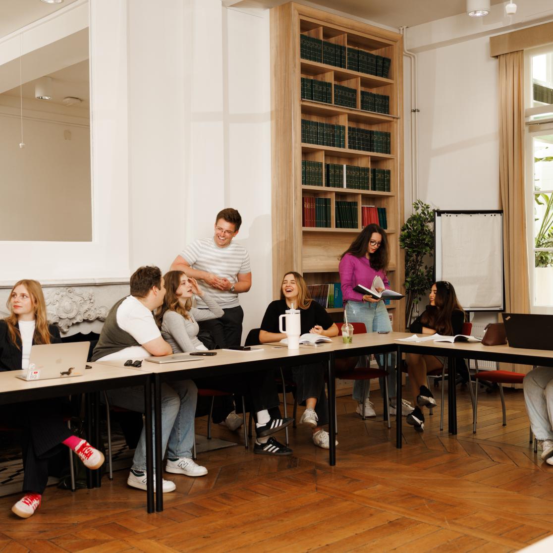 Studenten zitten in de Spiegelzaal van de faculteit in een informele opstelling, waar ze samen lachen, overleggen en presenteren.