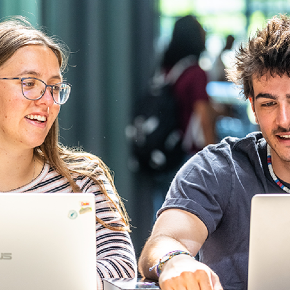 A guy and a girl, laughing together - both working on their laptop 