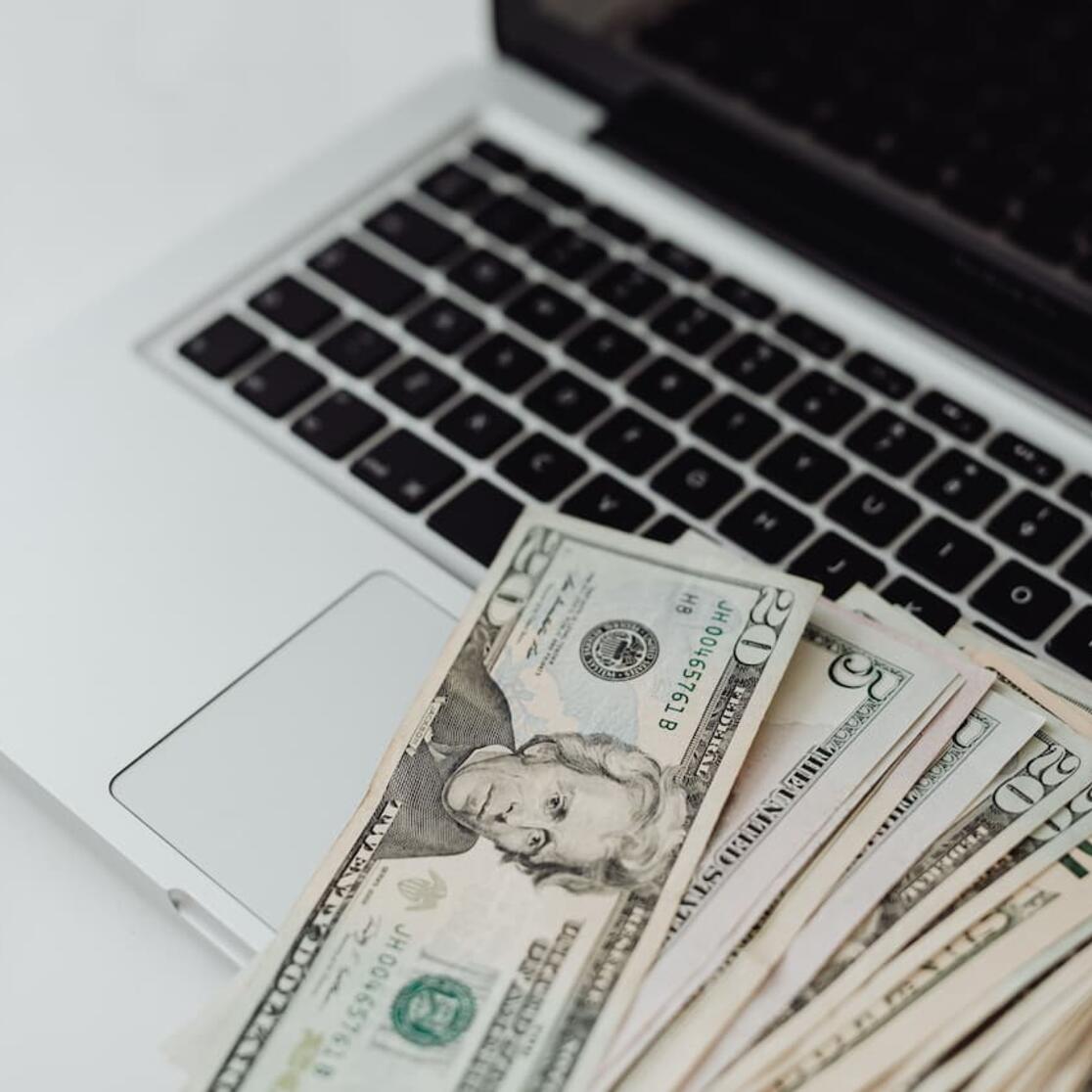 A laptop with a fan of cash money on it.