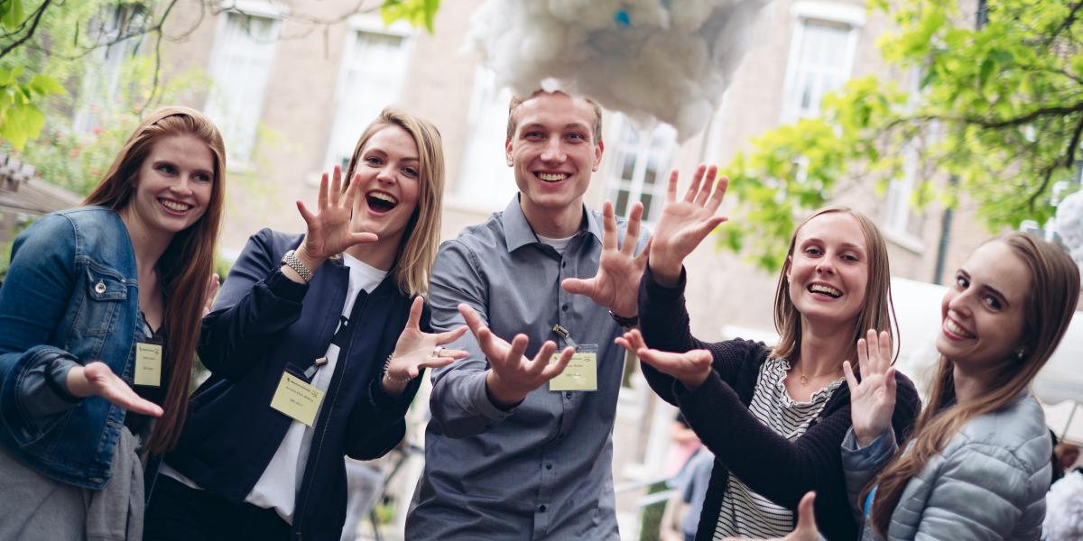 5 Students smiling at the camera and throwing something in the air at Alumni day