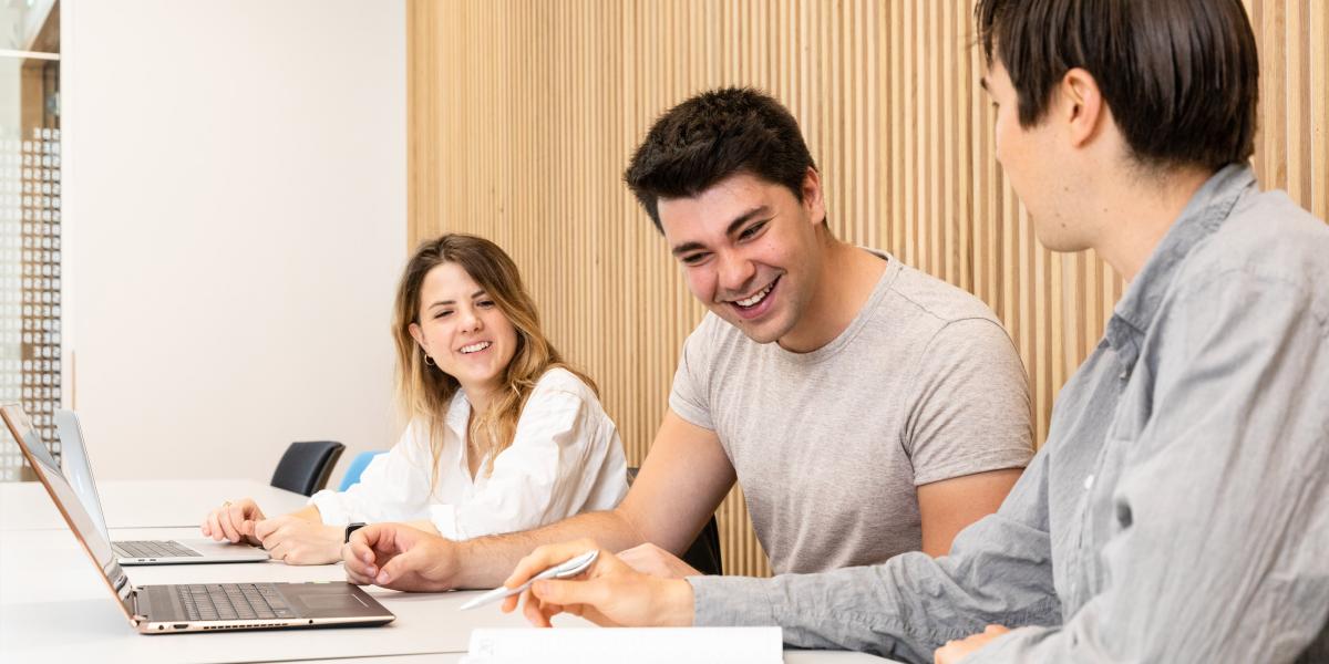 3 students interacting with eachother at a table in a classroom
