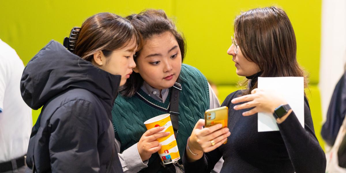Three students looking at a phone together, engaged in discussion
