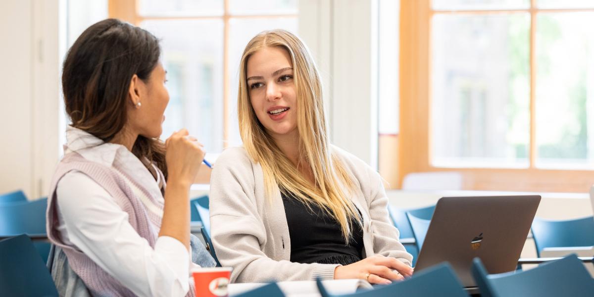 Two students sitting in a lecture hall, engaged in a discussion