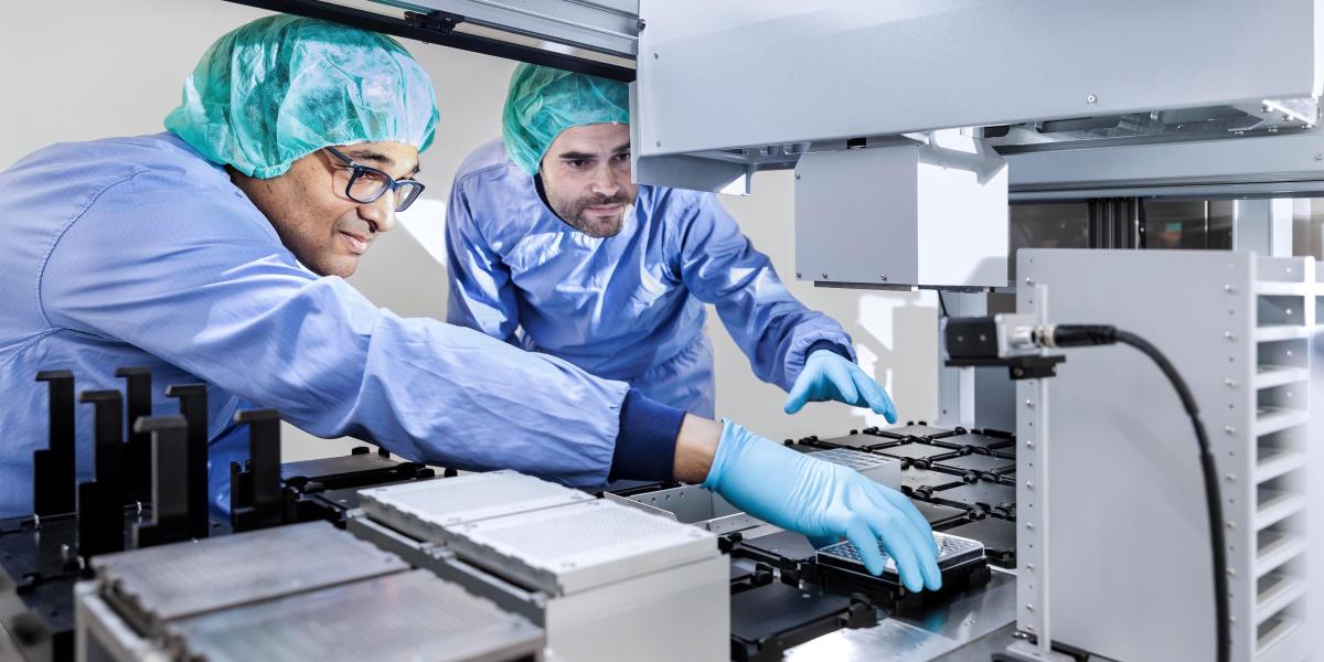 Two researchers in protective wear reaching into a machine