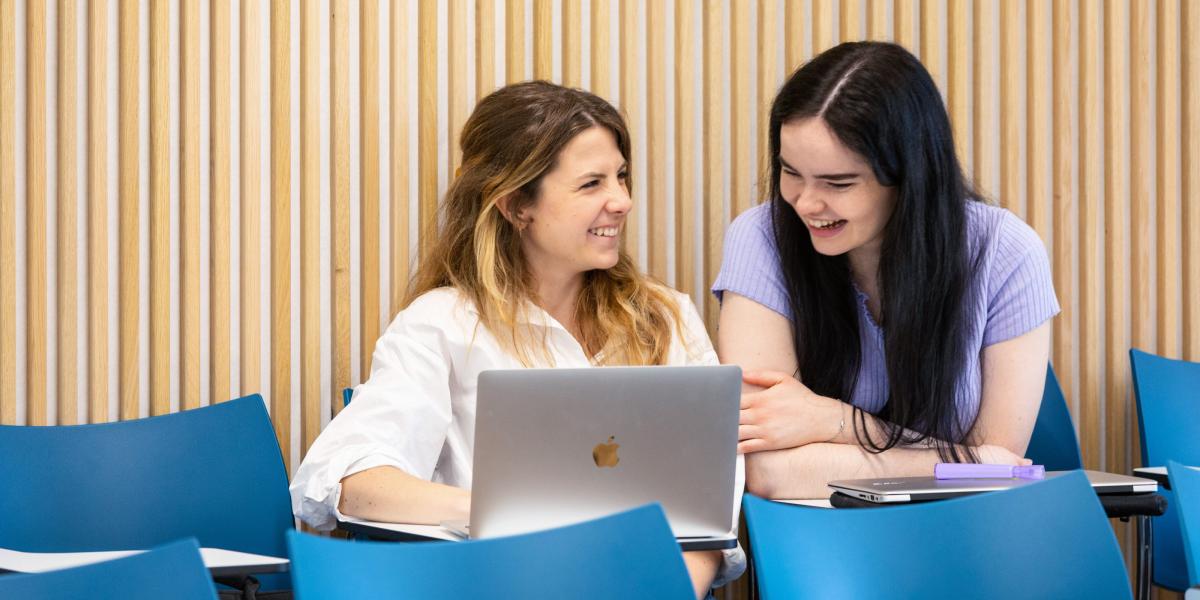 Two seated researchers with one laptop laughing