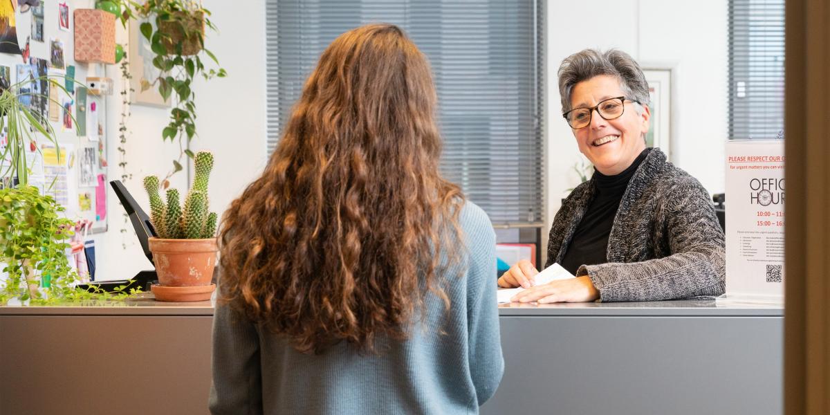 Someone at a reception smiling at a student at the desk