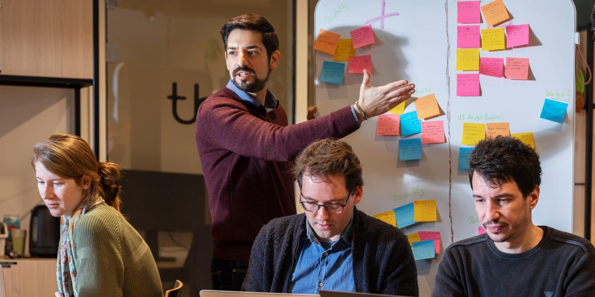 Someone in front of a board with sticky notes, talking to others in the room 