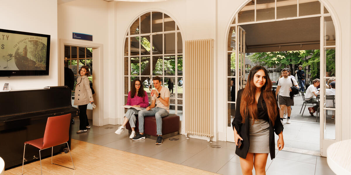 Students at the Faculty of Law’s Law Café: one student walks in while others are seated inside and outside, studying and relaxing.