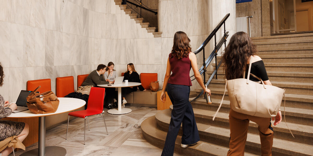 Students working and chatting in the marble hallway of the Lenculenhal, with seating along the wall and a grand staircase in view.