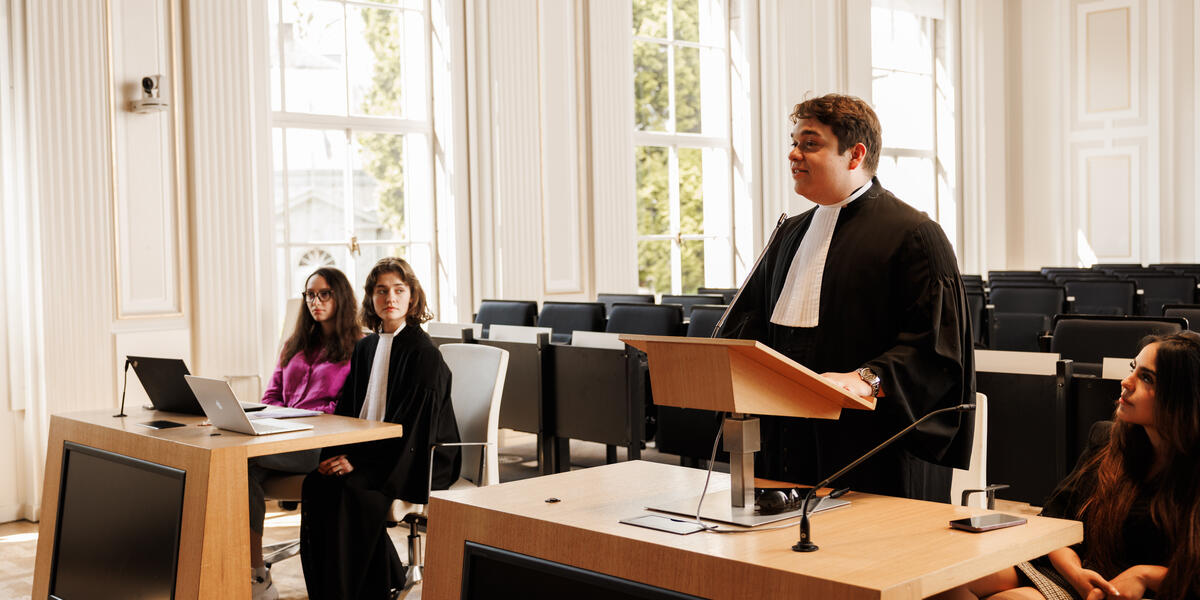 Studenten oefenen een rechtszaak in toga tijdens een moot court-sessie aan de rechtenfaculteit van Maastricht University, in een lichte zaal met grote ramen.