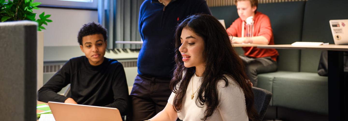 Three students are discussing something at a laptop in the faculty’s learning space, while others work independently in the background.