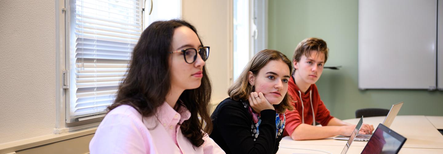 Three students listen attentively during a PBL session in a faculty tutorial room.