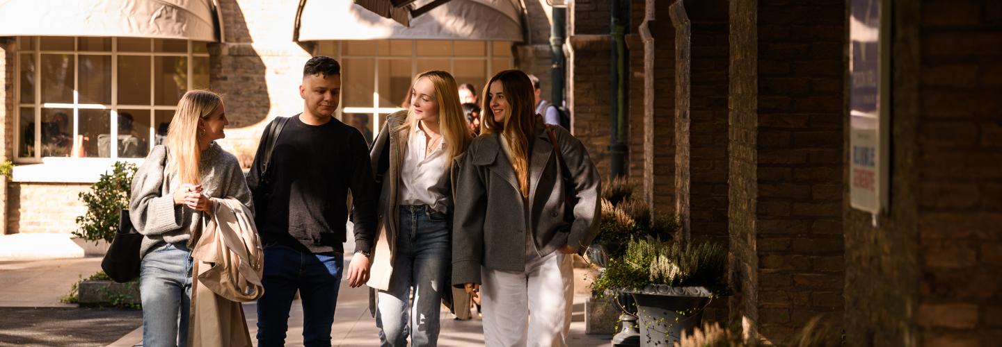 Four students walk together through the faculty’s courtyard, chatting in the sunlight.