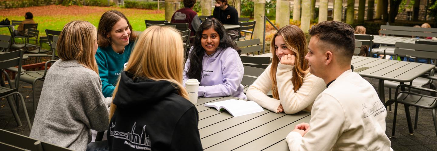 Students sit together at a table in the faculty garden, laughing during an informal study discussion.