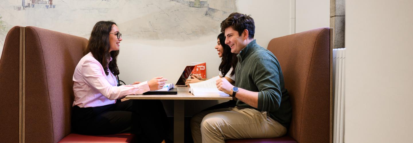 Three students sit together in a booth in the faculty’s learning space, discussing study materials.