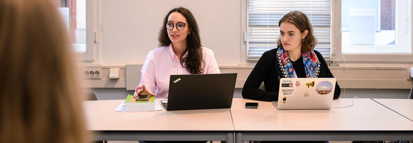 Two students sit at the table during a PBL session, attentively listening to a group member outside the frame.