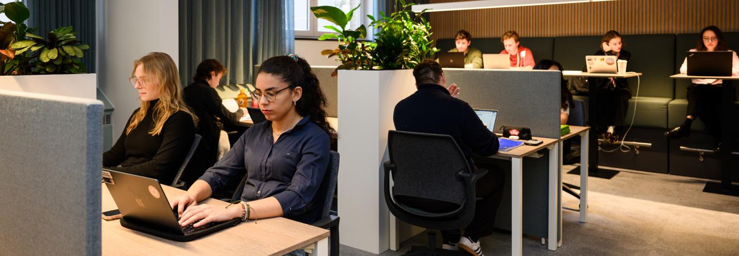 Students working quietly at individual desks and group benches in the faculty’s learning space.