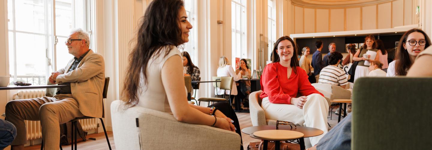 Studenten en staf in gesprek en ontspannen sfeer in de common room van de rechtenfaculteit, met hoge ramen, warme verlichting en een karakteristiek houten plafond.