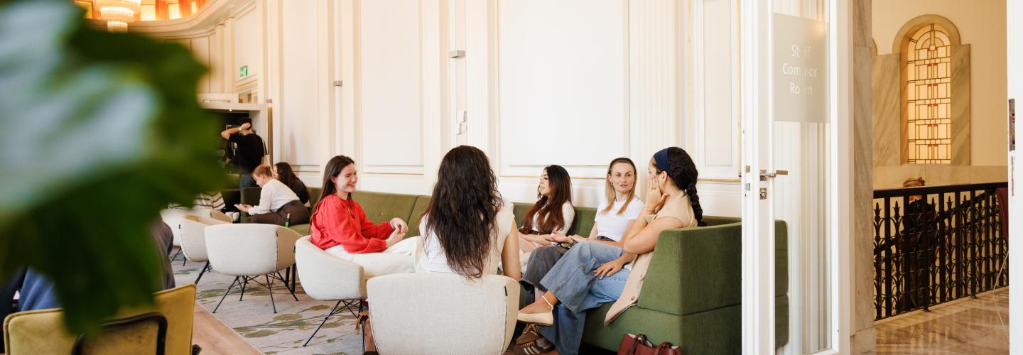 Students relaxing and chatting in the Faculty of Law's Common Room, featuring the iconic wooden ceiling and chandeliers.